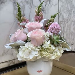 Pink roses and white hydrangeas arranged in a white vase with a face design.