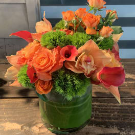Orange roses and calla lilies in a green glass vase