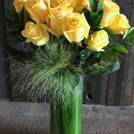 Yellow roses arranged in a tall green vase with grassy filler