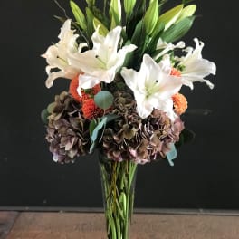 Tall bouquet of white lilies and hydrangeas in a clear glass vase