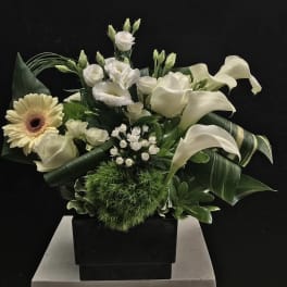 White floral arrangement with calla lilies, roses, and a gerbera daisy in a black vase