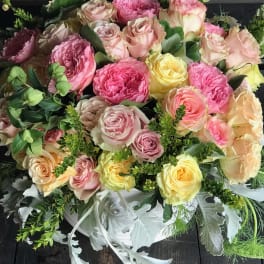 Bouquet of pink, peach, and yellow roses with greenery in a white container