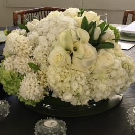White floral centerpiece with roses and hydrangeas on a dining table