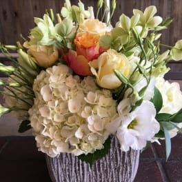 Mixed bouquet of cream and peach flowers in a ribbed white vase