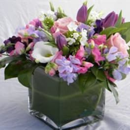 Mixed pink, purple, and white flowers in a square glass vase