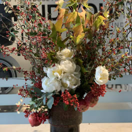 Tall arrangement of white flowers and red berry branches in a dark vase