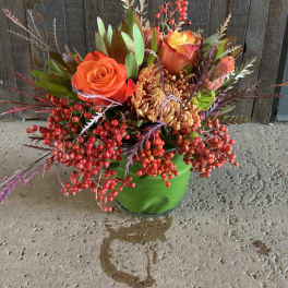 Orange roses and mums in a green vase with red berries