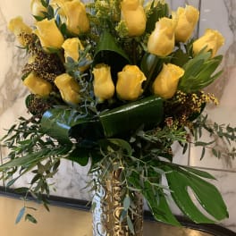 Yellow roses arranged in a gold vase with mixed greenery