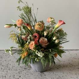 Mixed peach and coral flowers arranged in a gray pot