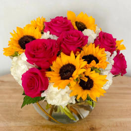 Bouquet of hot pink roses, sunflowers, and white hydrangeas in a glass vase