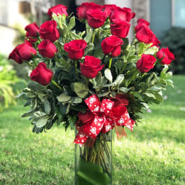 Bouquet of red roses in a tall glass vase with a red heart ribbon