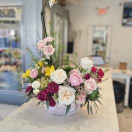 Mixed pink, white, and yellow roses in a low arrangement with a tall white orchid stem