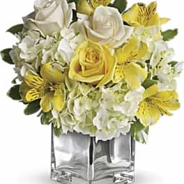 Yellow and white floral arrangement in a clear square vase
