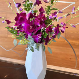 Purple orchid arrangement in a tall white vase