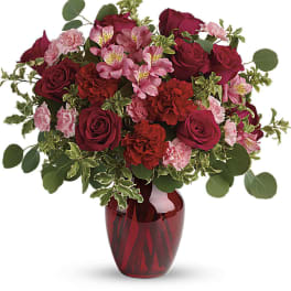 Red roses and pink flowers arranged in a red glass vase