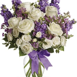 White roses and purple flowers in a glass vase with a purple ribbon