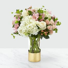 Pink and white bouquet in a clear vase with a gold base