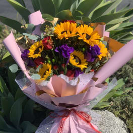 Bouquet of sunflowers and purple flowers wrapped in pink paper