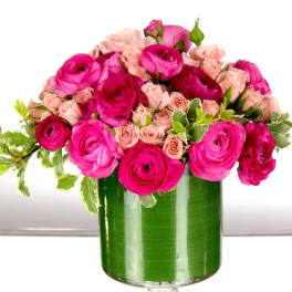 Pink ranunculus and pale pink spray roses in a leaf-lined clear glass cylinder vase