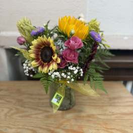 Mixed bouquet with sunflowers, pink blooms, and purple flowers in a glass jar