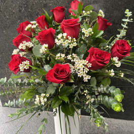 Red roses arranged in a white vase with white filler flowers and greenery