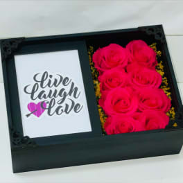 Black gift box with hot pink roses beside a card reading live laugh love