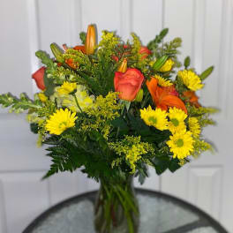 Bouquet of orange roses, yellow daisies, and lilies in a glass vase