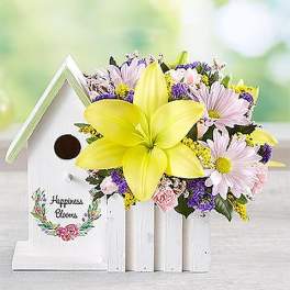 Bouquet with a large yellow lily and pastel daisies beside a white birdhouse