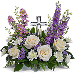 White roses and purple flowers arranged around a silver cross