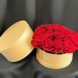 Red roses arranged in a round gold gift box with the lid beside it
