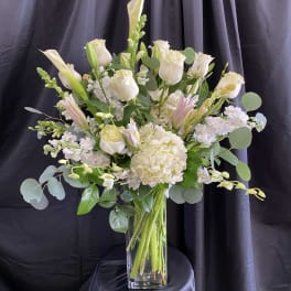 White roses and lilies arranged in a tall glass vase