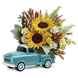 Blue toy truck filled with sunflowers and white flowers
