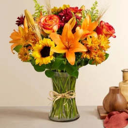 Bouquet of orange lilies, roses, and sunflowers in a glass vase
