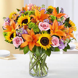 Mixed bouquet of sunflowers, orange lilies, and pink roses in a glass vase