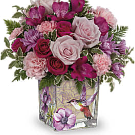 Pink and magenta bouquet in a square glass vase with a hummingbird design