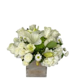 White floral arrangement in a square vase with lilies and daisies