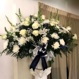 Large white floral arrangement in a pedestal vase with a ribbon bow