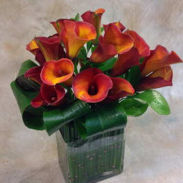 Arrangement of red and orange calla lilies in a square glass vase