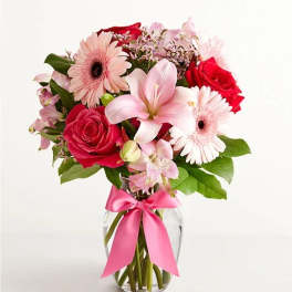 Pink and red mixed bouquet in a clear glass vase with a pink ribbon