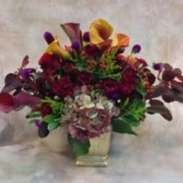 Mixed bouquet with calla lilies and dark purple flowers in a square vase