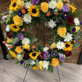 Heart-shaped floral wreath with roses, sunflowers, and white daisies on a stand