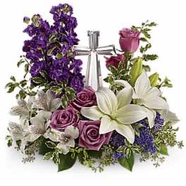 Purple and white floral arrangement with roses and lilies around a silver cross