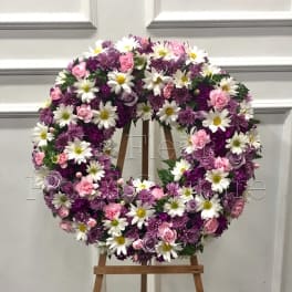 Round floral wreath of pink, purple, and white flowers on a wooden easel