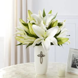White lilies arranged in a tall vase with a cross emblem