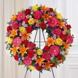 Colorful floral wreath on a black stand with roses, lilies, and daisies