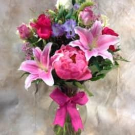 Pink lilies and roses in a glass vase with a bright ribbon