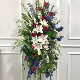 Tall standing floral spray with red roses, white lilies, and blue flowers