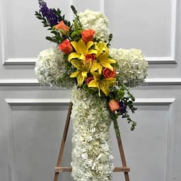 Cross-shaped floral arrangement with white hydrangeas, yellow lilies, and orange roses