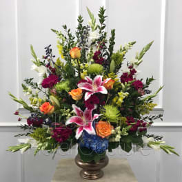 Tall mixed floral arrangement with lilies, roses, and chrysanthemums in a bronze vase