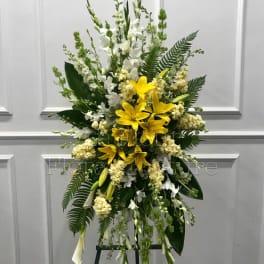 Standing floral spray with yellow lilies and white flowers on an easel